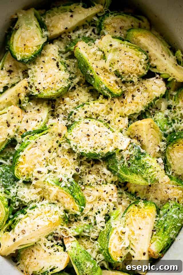 Finished dish: tender Brussels sprouts liberally coated with savory Parmesan cheese. Close-up of tender, slow-cooked Brussels sprouts beautifully topped with generous flakes of Parmesan cheese, glistening with melted butter.