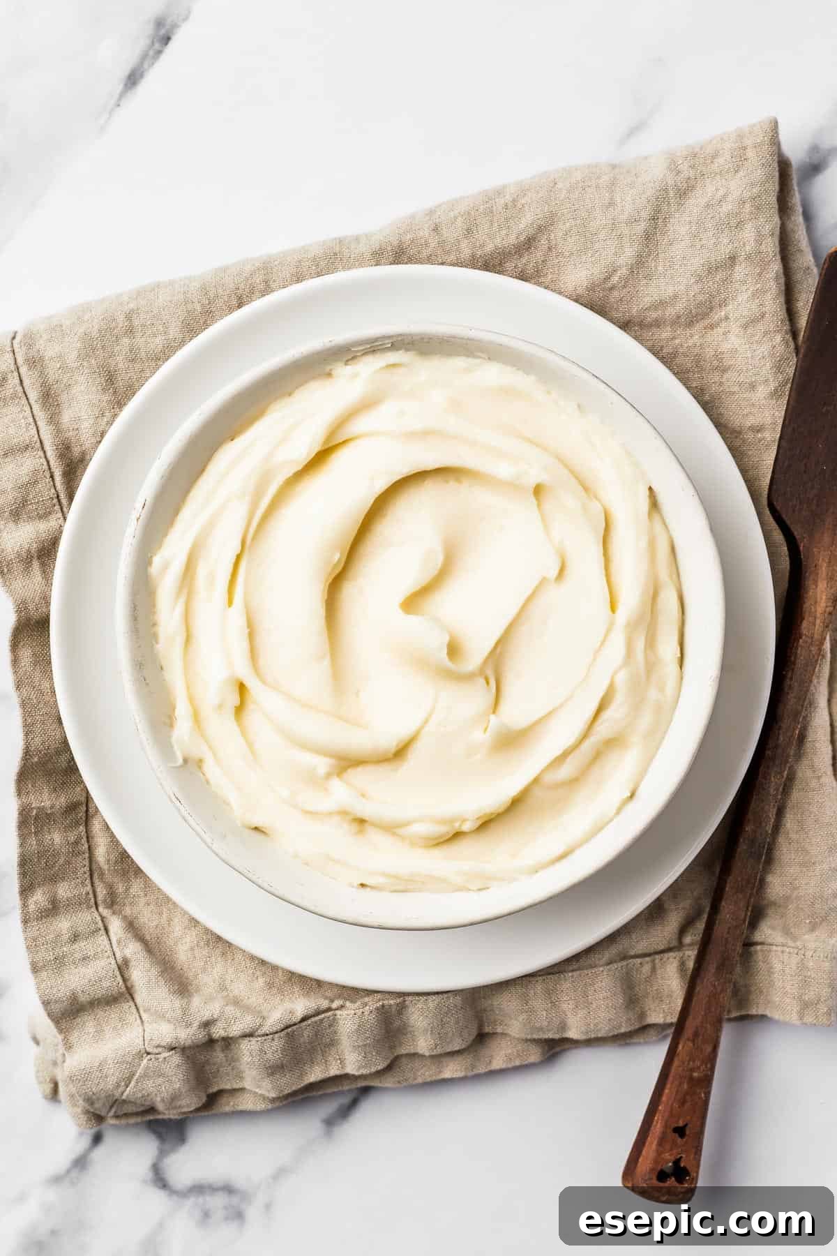 A beautifully composed shot of a bowl of creamy white cream cheese icing resting on a textured linen napkin, ready to be used.