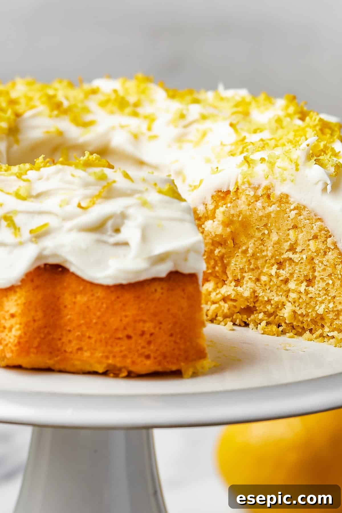 Close-up shot of a beautiful lemon bundt cake, generously iced with thick, creamy frosting and garnished with delicate strands of lemon zest.