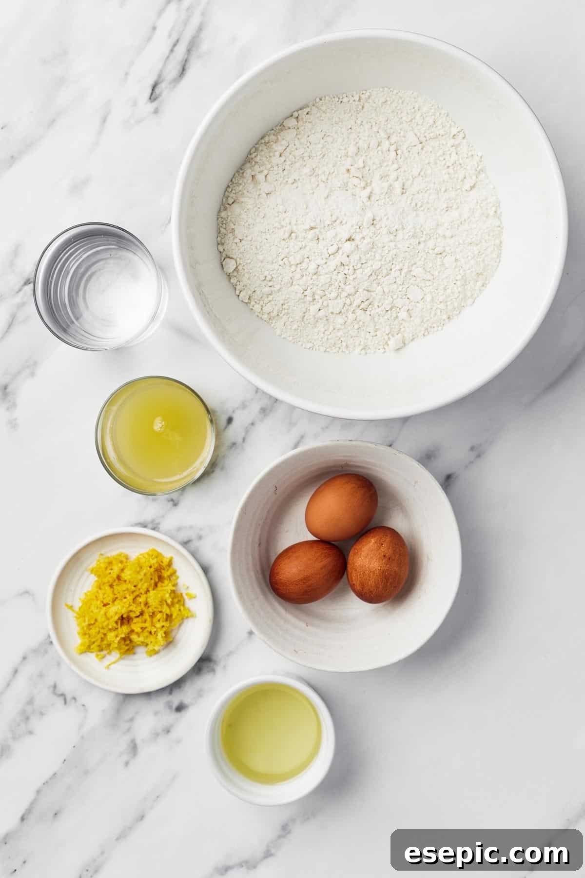 A top-down view showcasing the essential ingredients for lemon bundt cake: a glass of water, a box of cake mix, cooking oil, three fresh eggs, vibrant lemon zest, and a small bowl of fresh lemon juice, neatly arranged.