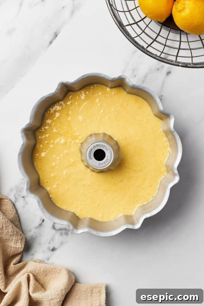 A close-up view of a Bundt pan filled with smooth, bright yellow lemon cake batter, ready for baking.