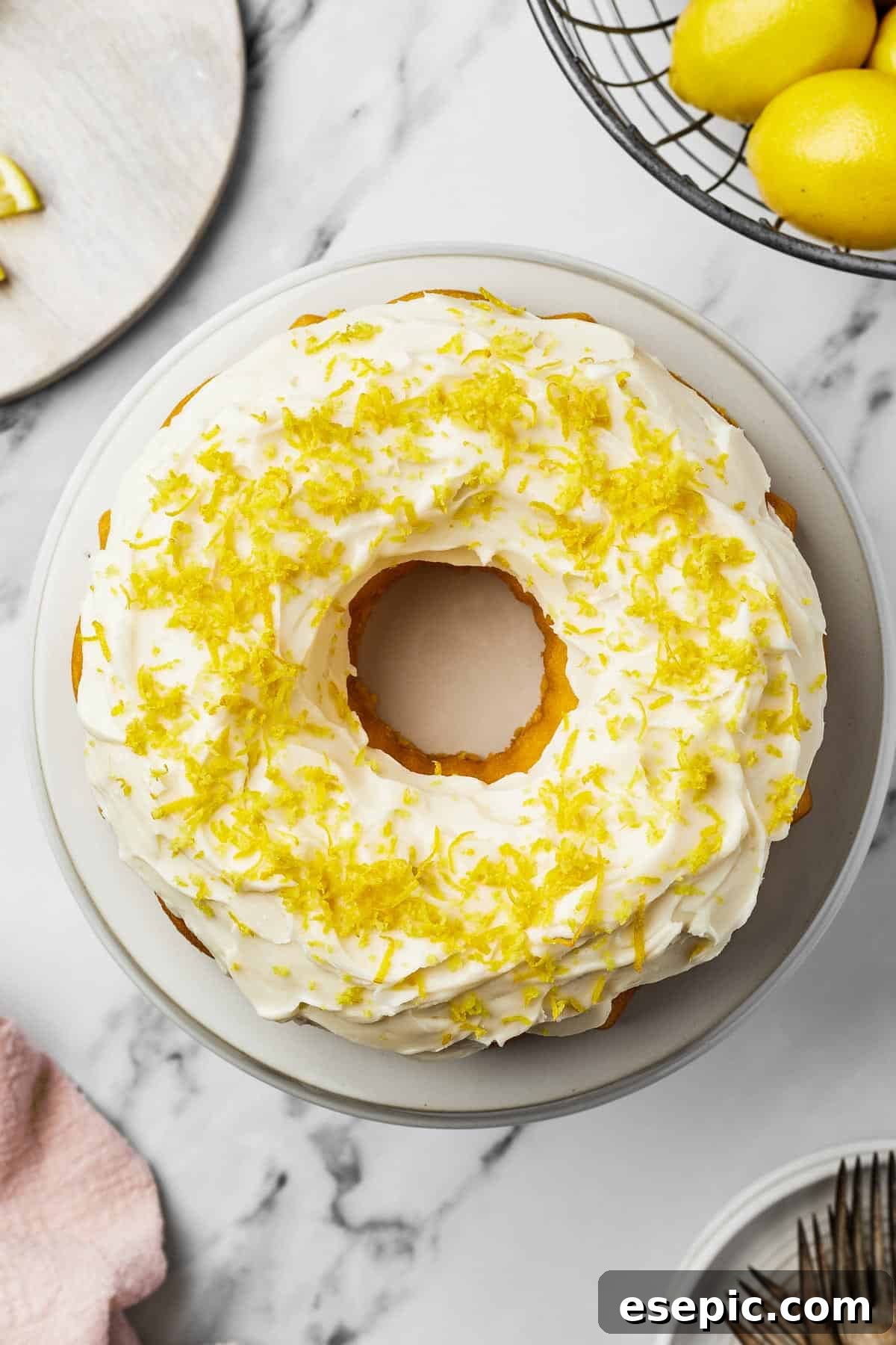 A beautifully decorated lemon bundt cake with smooth white frosting and vibrant lemon zest, presented on a round white cake plate.