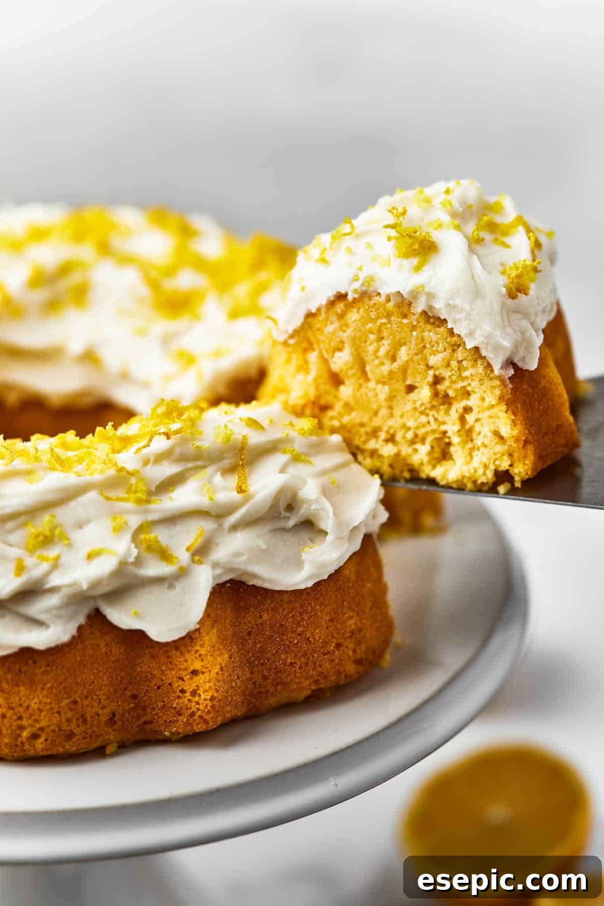 A lemon Bundt cake on a serving platter, with a single slice being carefully lifted away using a cake server, ready to be enjoyed.