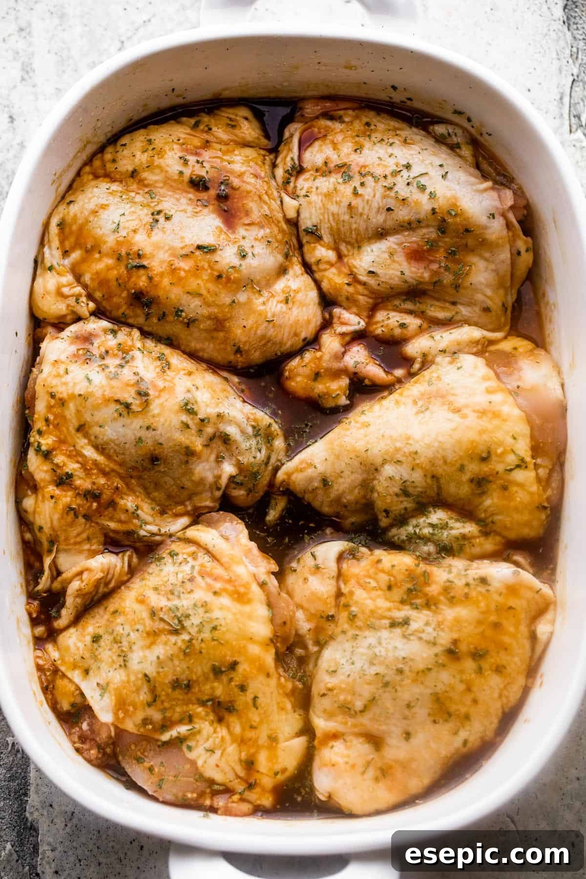 Overhead image of a white baking dish with six raw bone-in, skin-on chicken thighs arranged inside of the baking dish.