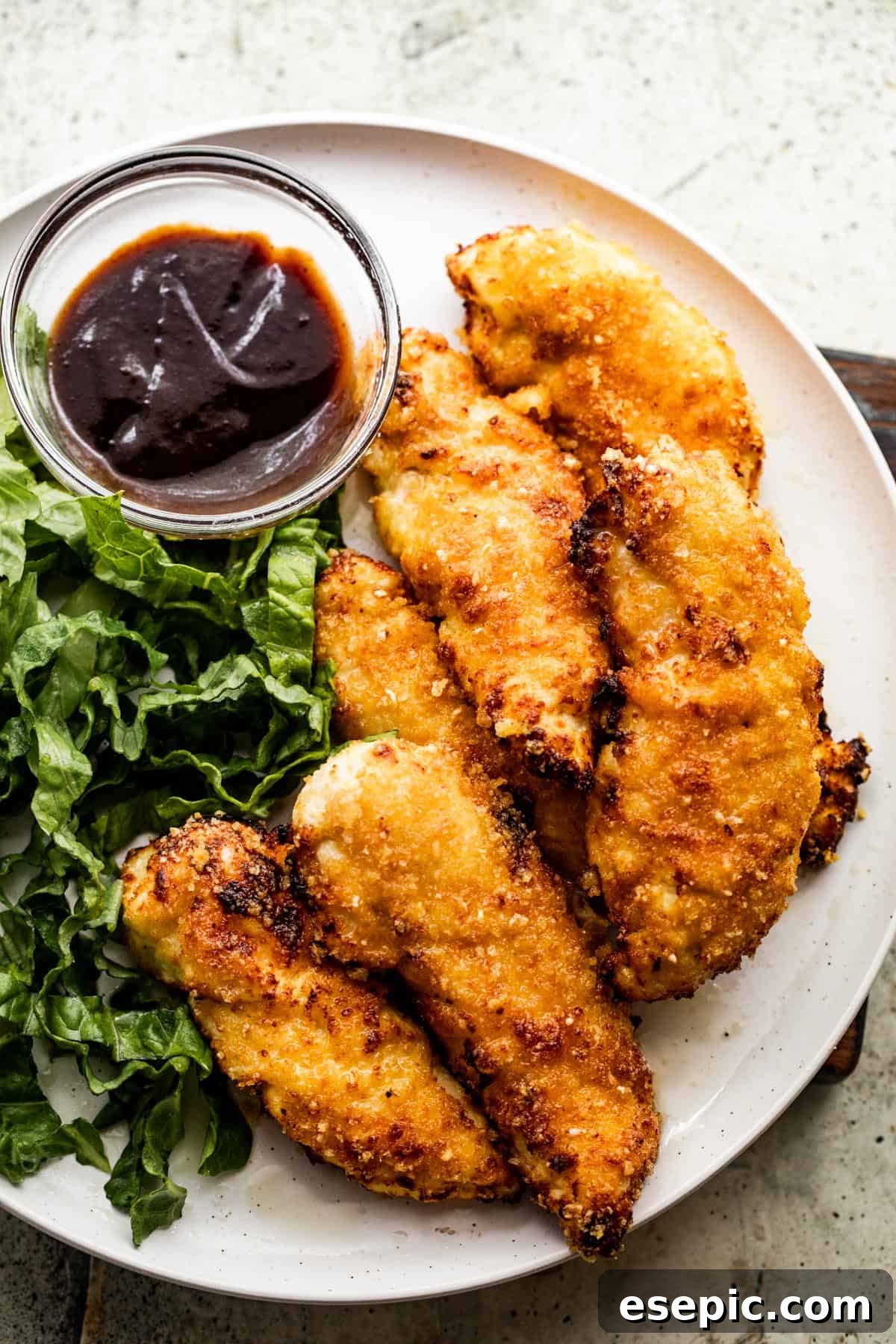 A beautifully arranged dinner plate featuring golden-brown, crispy air fryer chicken tenders alongside fresh green salad and a dollop of barbecue sauce.