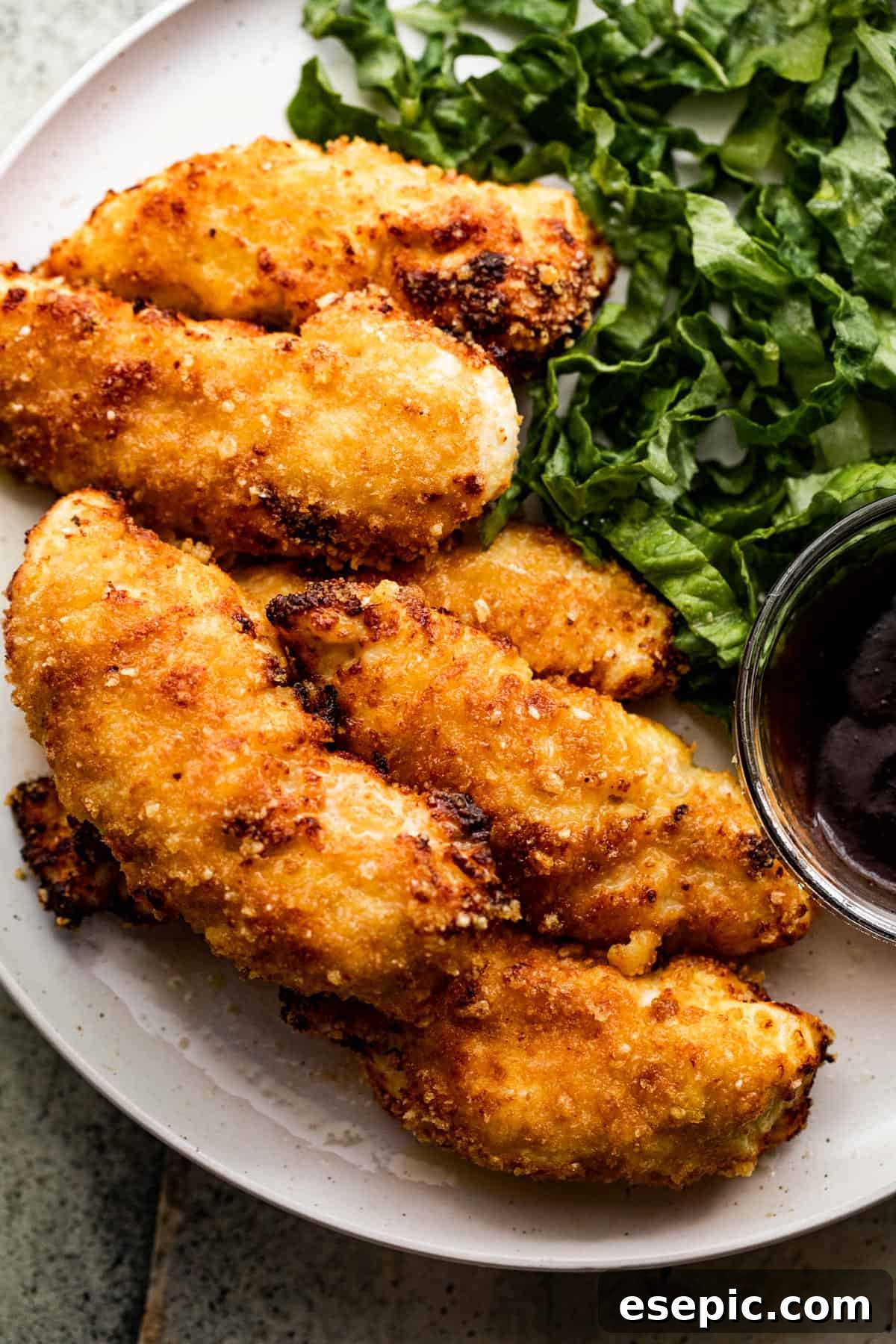A close-up, overhead view of a dinner plate showcasing perfectly cooked air fryer chicken tenders, accompanied by fresh greens and a side of smoky barbecue sauce.