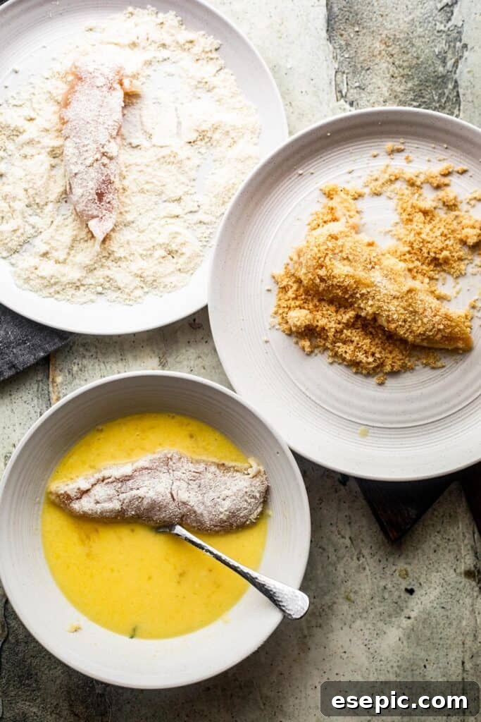Bottom left: a raw chicken tender soaking in a bowl with whisked eggs. Upper left: a raw chicken tender in a bowl with all-purpose flour. Right side: a raw chicken tender generously coated in pork rind breading, illustrating the breading process.