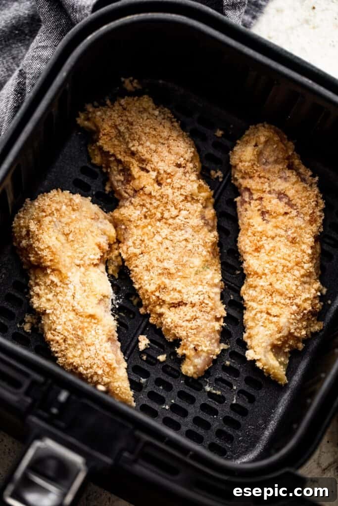 Three raw, perfectly breaded chicken tenders neatly arranged inside a black air fryer basket, ready for cooking.
