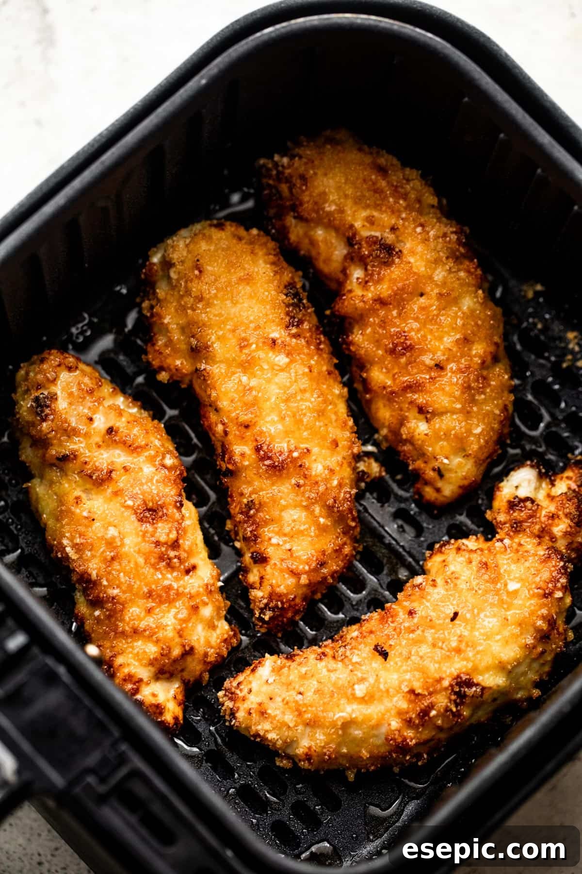 Four perfectly breaded and cooked golden-brown chicken tenders arranged invitingly inside a black air fryer basket, showing their crispy texture.