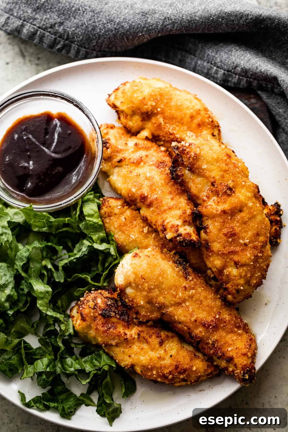 A perfectly portioned dinner plate featuring golden-brown air fryer chicken tenders, a vibrant green side salad, and a ramekin of savory barbecue sauce.