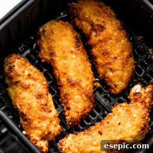 Four breaded and cooked golden-brown chicken tenders arranged invitingly inside a black air fryer basket, showing their crispy texture.