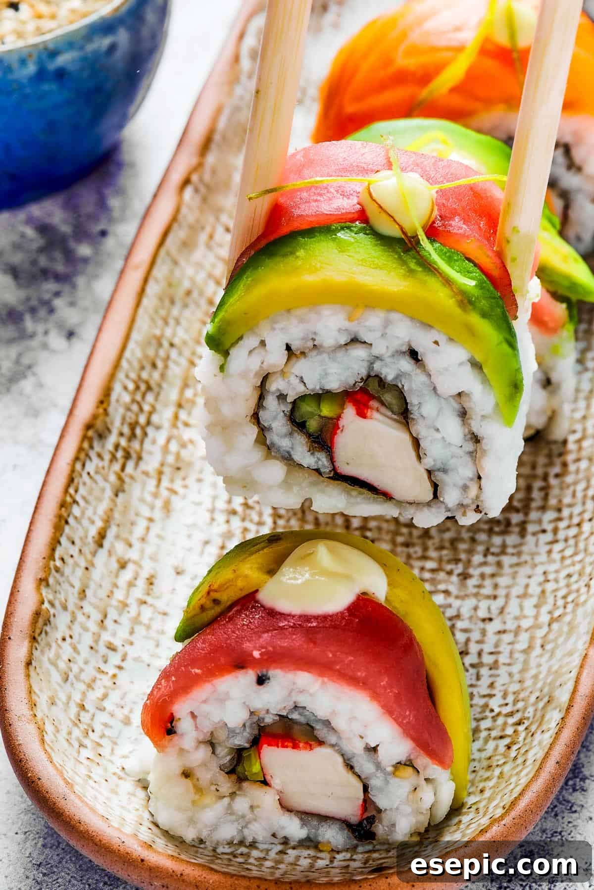 A bite of sushi held in a pair of chopsticks. A small plate of sushi and a container of soy sauce is in the background.