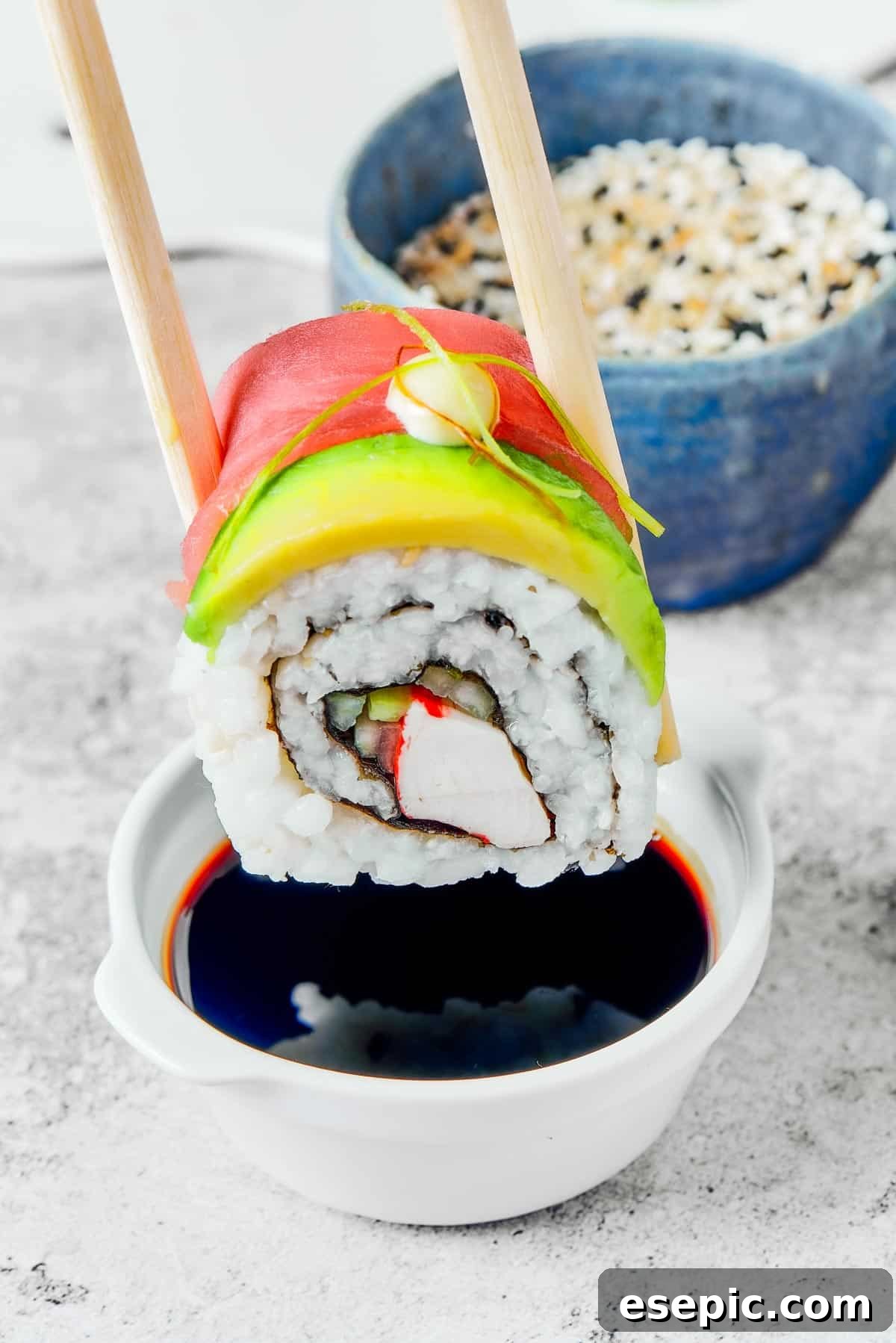 A close-up of a bite of Rainbow Roll sushi, composed of vibrant fish and avocado on rice, poised to be eaten. In the background, a small plate holds more sushi pieces, and a bottle of soy sauce sits ready, highlighting the deliciousness of the meal.