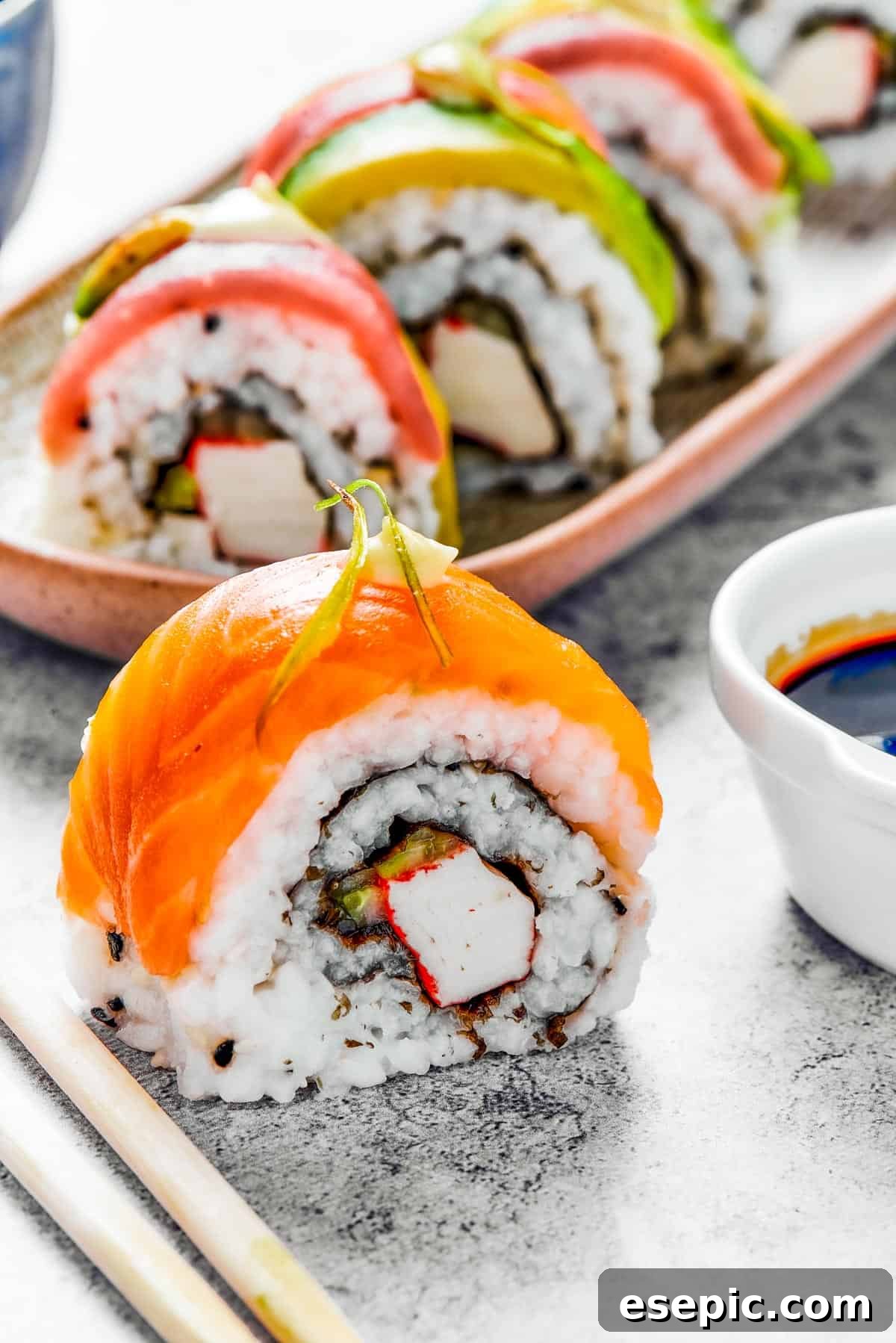 A bite of sushi set on a surface. A small plate of sushi and a container of soy sauce is in the background.