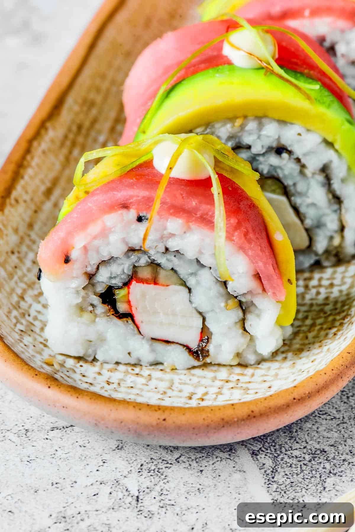 Close-up shot of sushi topped with salmon, avocado, mayonnaise, and pickled ginger.