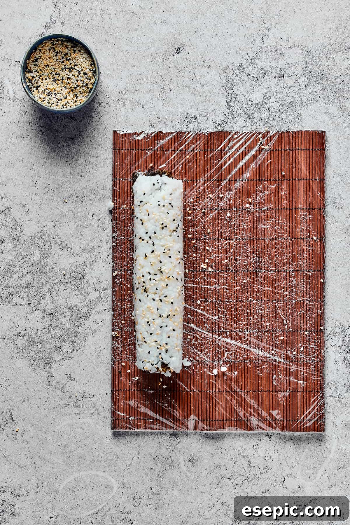 A partially rolled sushi roll rests on a bamboo mat, with the nori and rice firmly enclosing the inner fillings, demonstrating the technique used to create a tight and coherent sushi cylinder.