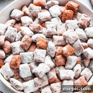 Close-up shot of puppy chow in a white bowl, to show the texture. Some pieces are fully coated in powdered sugar, while others are not.
