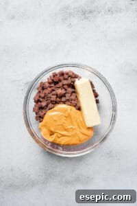 Peanut butter, chocolate chunks, and butter in a glass bowl.