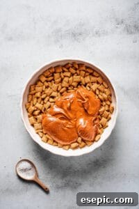 A large mixing bowl of Chex cereal, with a melted peanut butter chocolate mixture poured on top.
