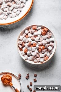 Muddy buddies in a white bowl, with a spoonful of peanut butter and a larger serving dish of the snack nearby.