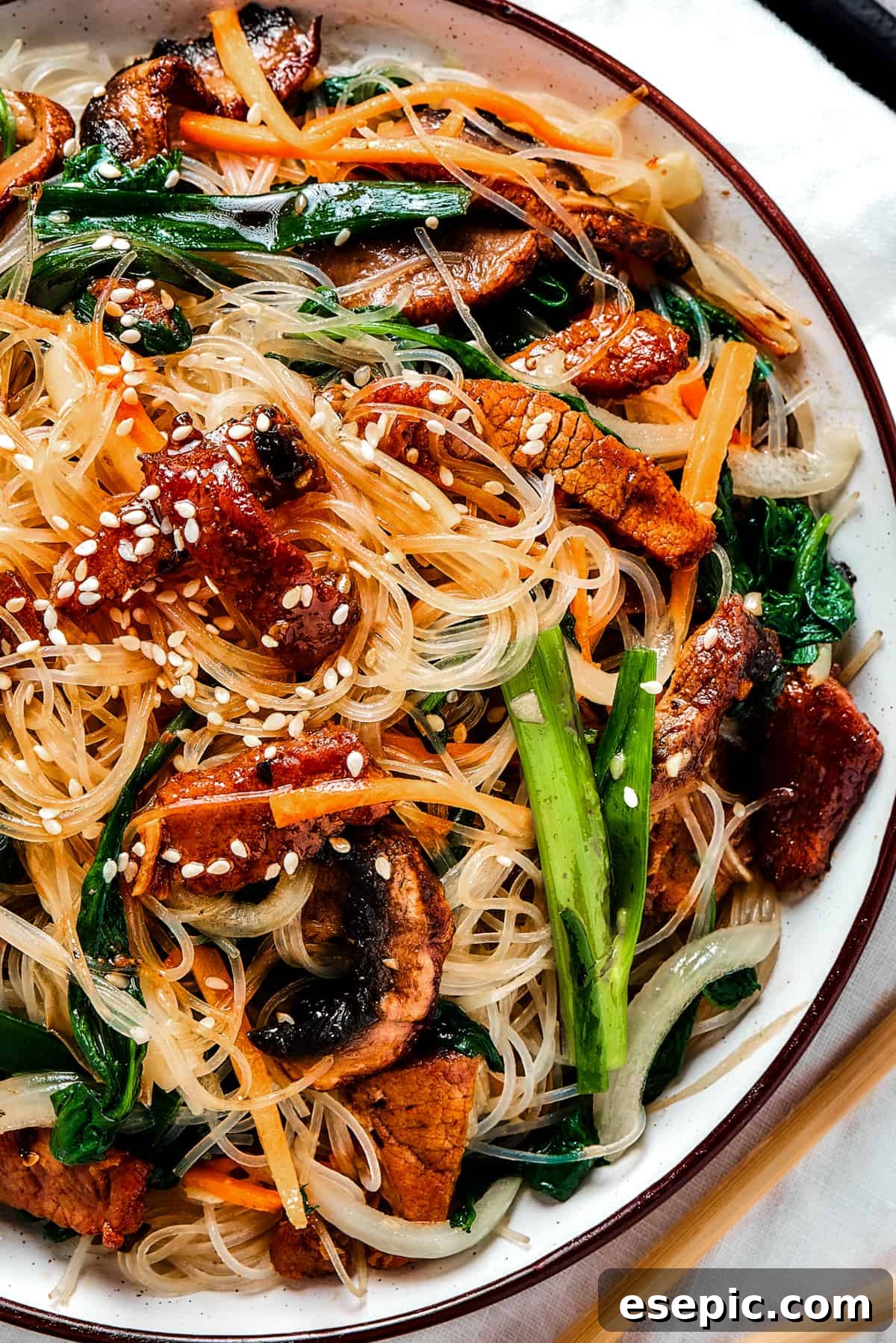 An overhead shot of a shallow dish of Beef Stir Fry with Glass Noodles (Japchae), beautifully garnished with toasted sesame seeds.