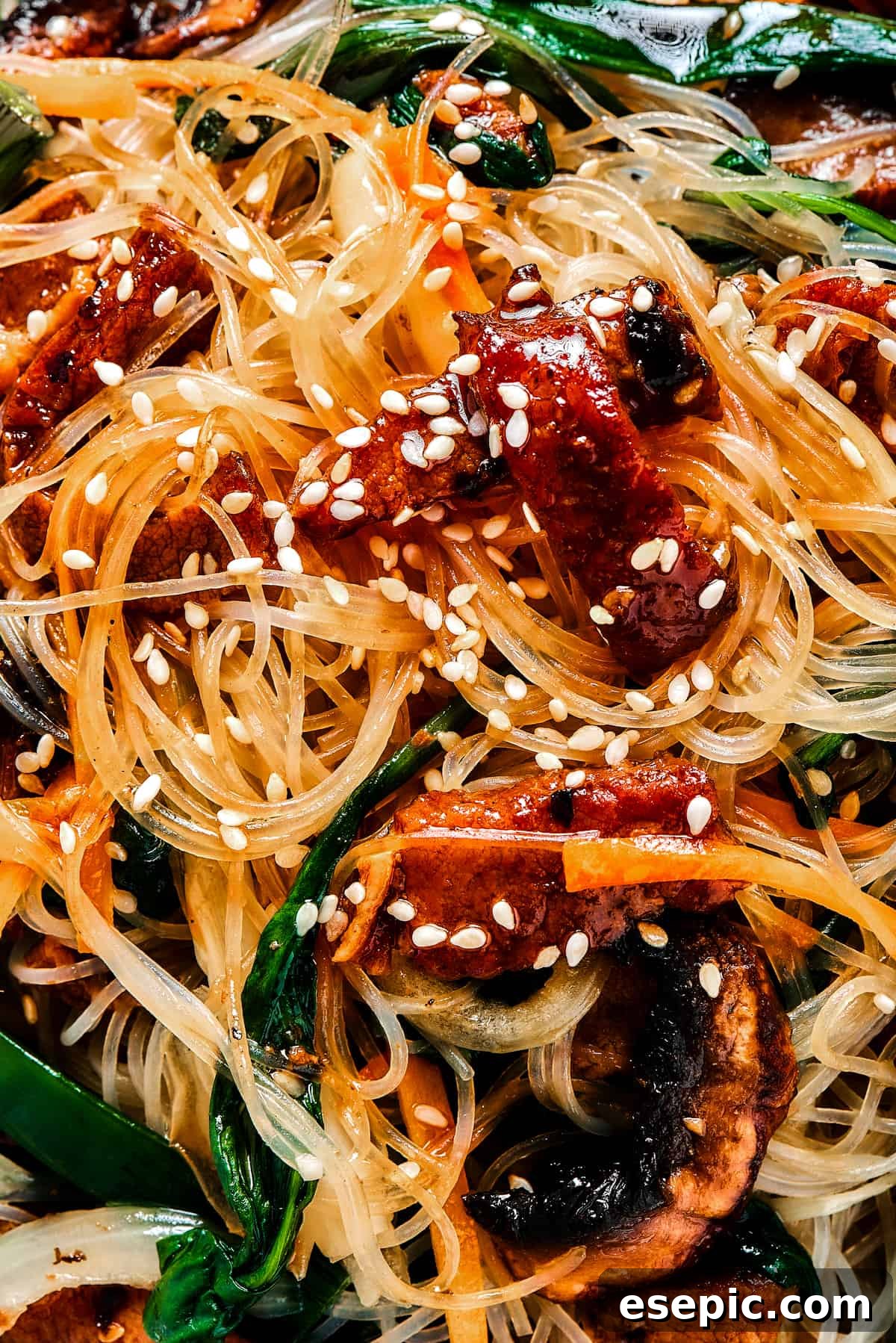 A close-up shot of Japchae (Korean glass noodle stir fry), artfully garnished with toasted sesame seeds, highlighting the vibrant colors and appealing textures of the dish.