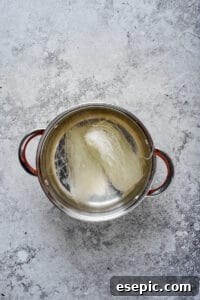 Glass noodles rehydrating in a stainless steel pot of hot water, showing their preparation before stir-frying.