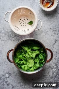 A pot of blanched spinach next to a colander, ready for draining and showing the vibrant green color achieved through blanching.