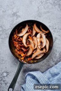 Beef and mushrooms simmering together in a skillet, illustrating the cooking process of the protein component.