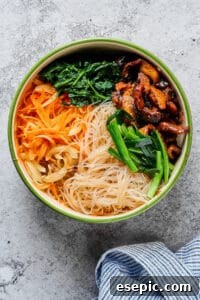 A large mixing bowl containing glass noodles, cooked beef, mushrooms, vibrant green onions, carrots, and spinach, showing the combined ingredients before final seasoning.