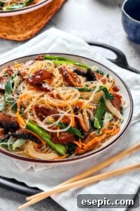 A beautifully presented serving bowl of Japchae (Korean glass noodle stir fry), complete with chopsticks, ready to be enjoyed.