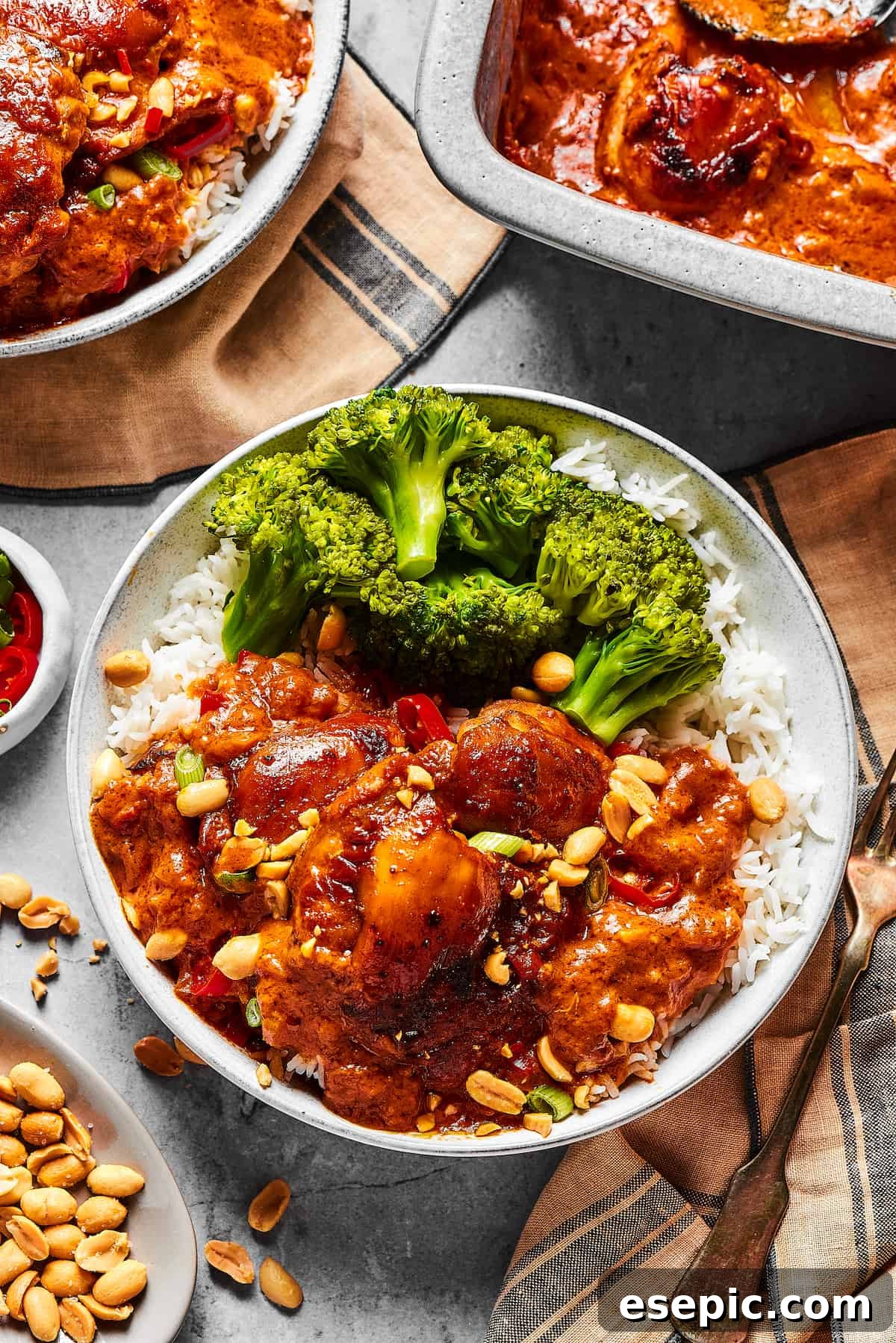 Simple Peanut Butter Chicken - Easy, Healthy, and Flavorful! Peanut chicken served with broccoli over rice. A baking dish of the chicken is nearby on the table, along with garnishes and more plates.