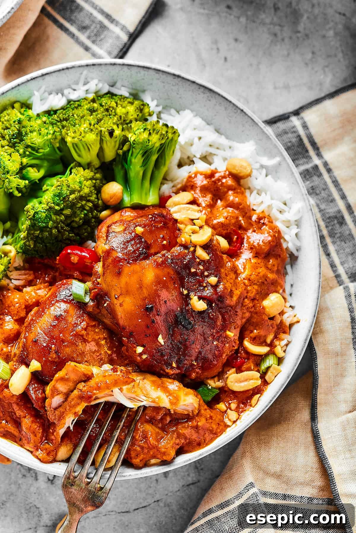 Simple Peanut Butter Chicken - Easy, Healthy, and Flavorful! overhead shot of a chicken thigh cooked in peanut sauce, with a fork pulling away a bite.