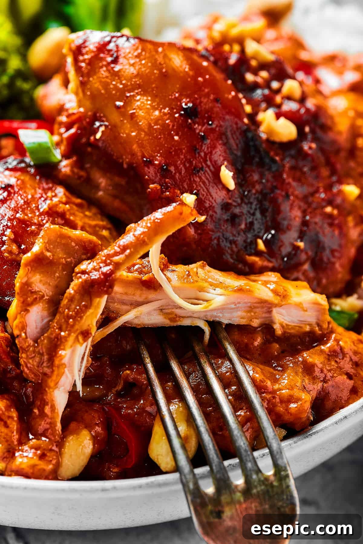 Simple Peanut Butter Chicken - Easy, Healthy, and Flavorful! A close-up shot of a chicken thigh cooked in peanut sauce, with a fork pulling away a bite.