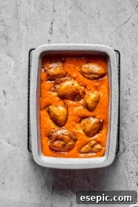 Creamy Peanut Chicken Delight 6 A baking dish full of creamy tomato peanut sauce, with chicken thighs arranged in the sauce.