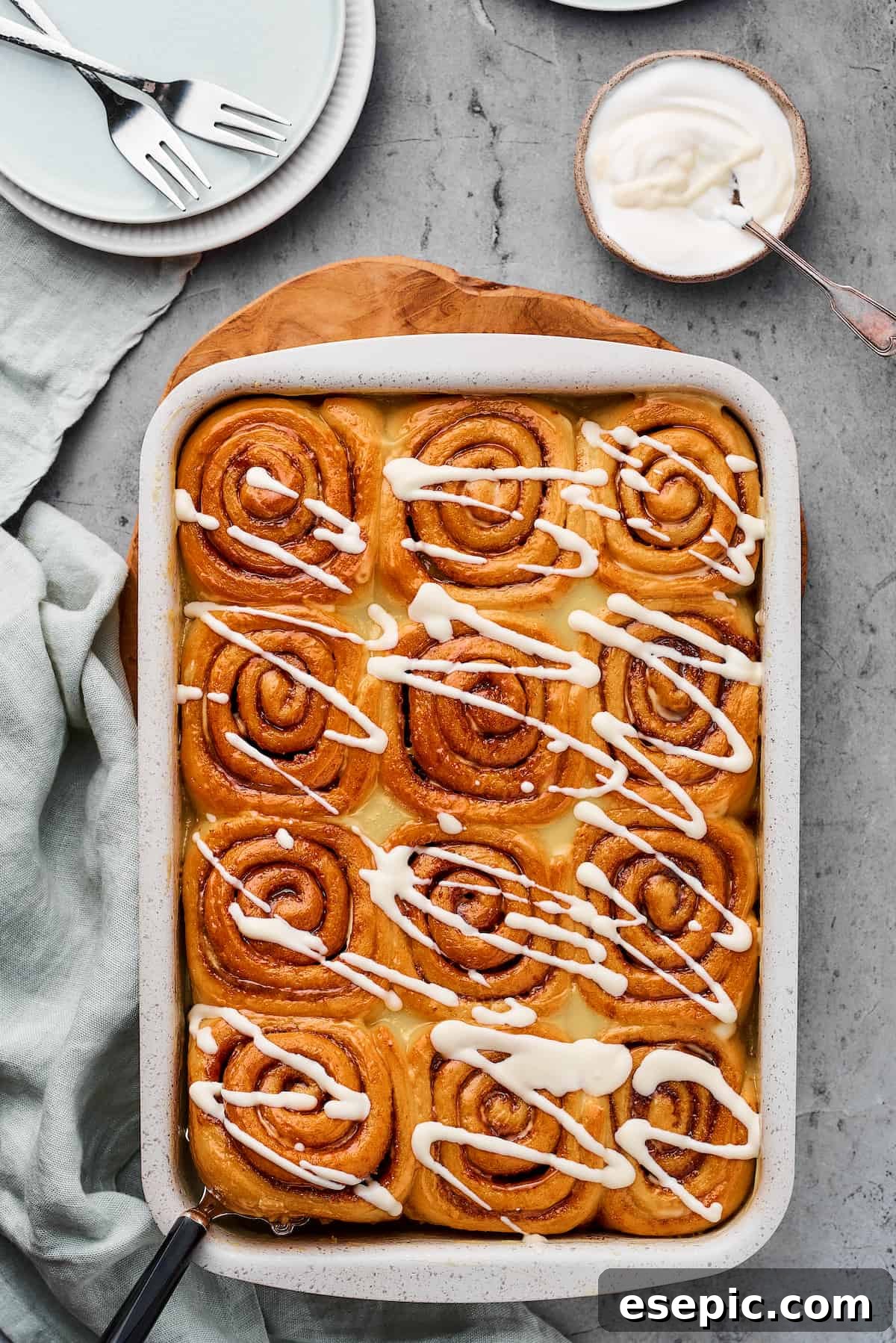 A pan of warm, baked cinnamon rolls, generously drizzled with a smooth white icing, ready to be served.