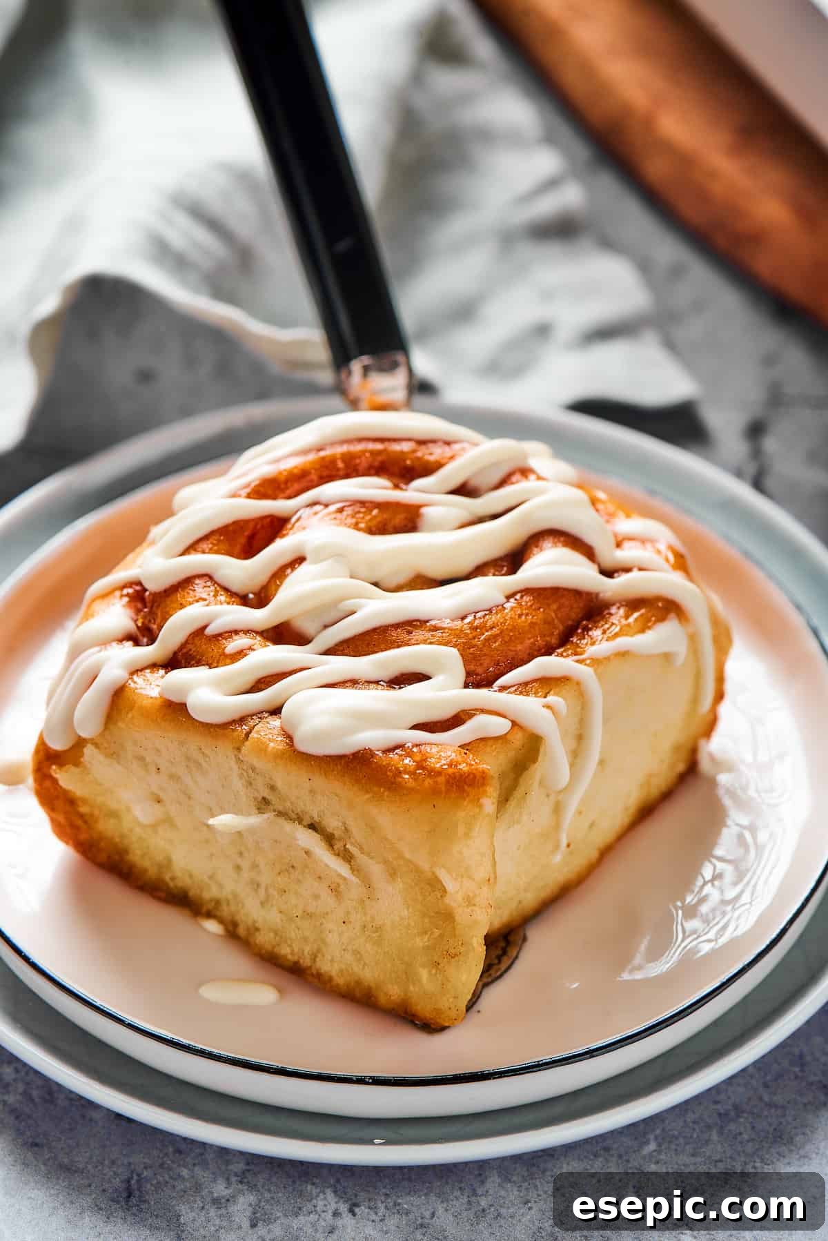 A fresh cinnamon bun on a small plate, with thick white glaze generously drizzled on top and a bite taken out.