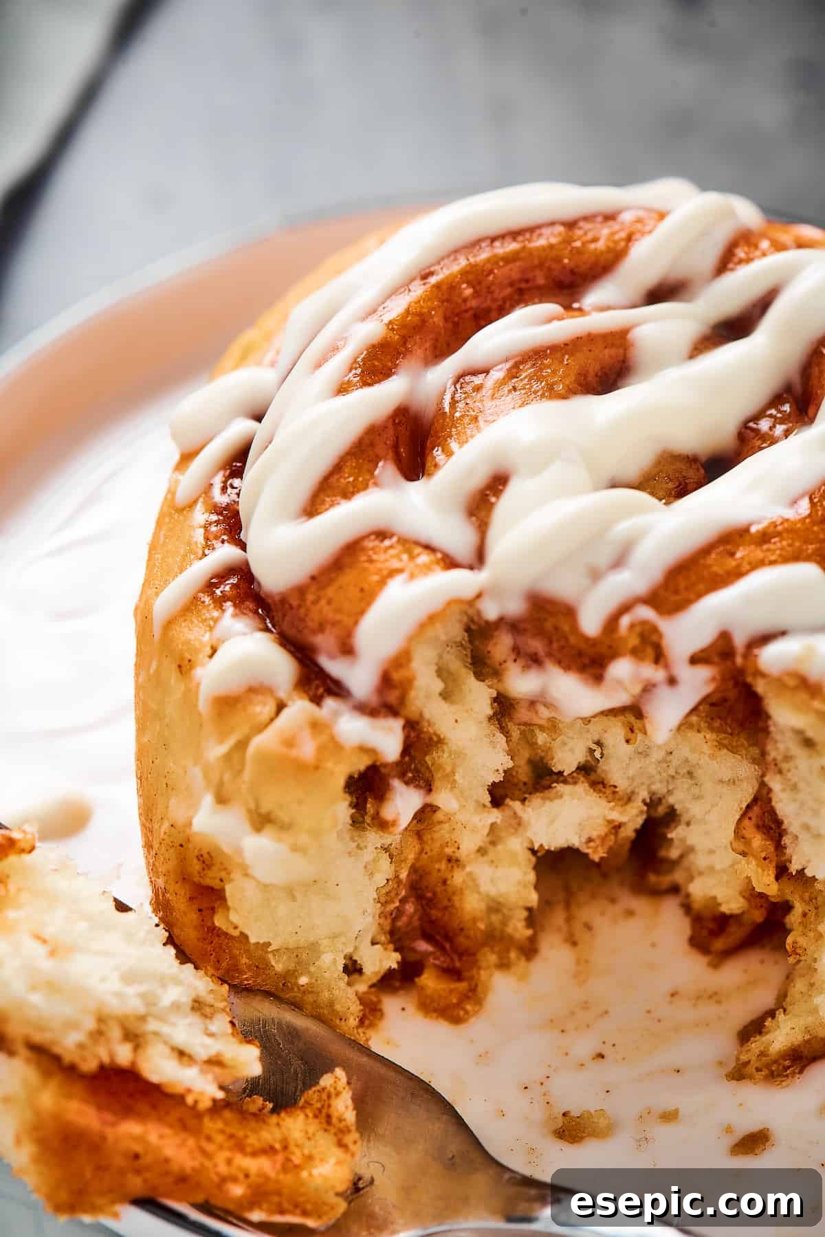 A fresh cinnamon roll with a bite taken from it, served on a small plate, revealing its soft, layered interior.