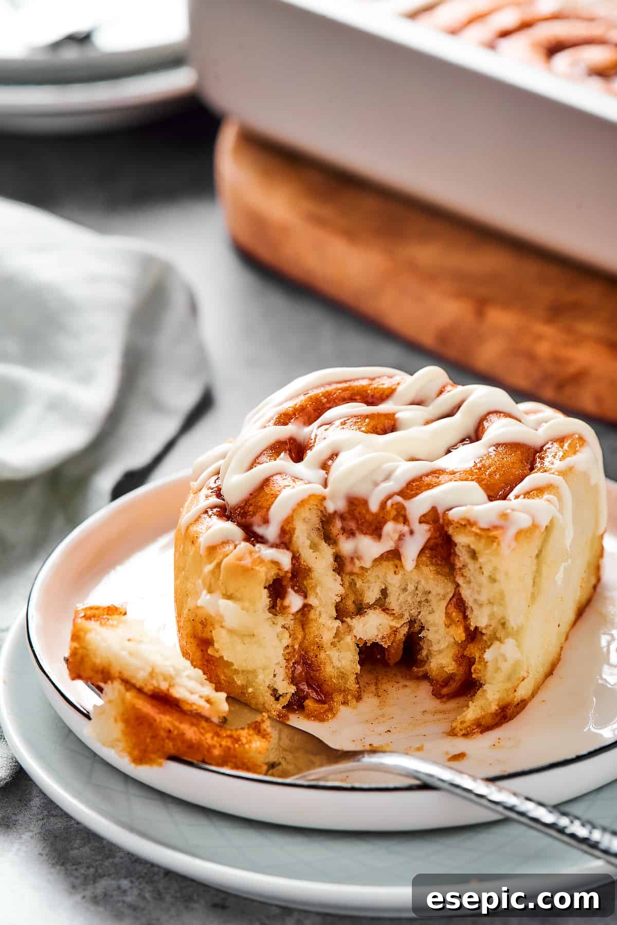 A bitten cinnamon bun on a small plate with a fork, revealing its soft, layered interior.