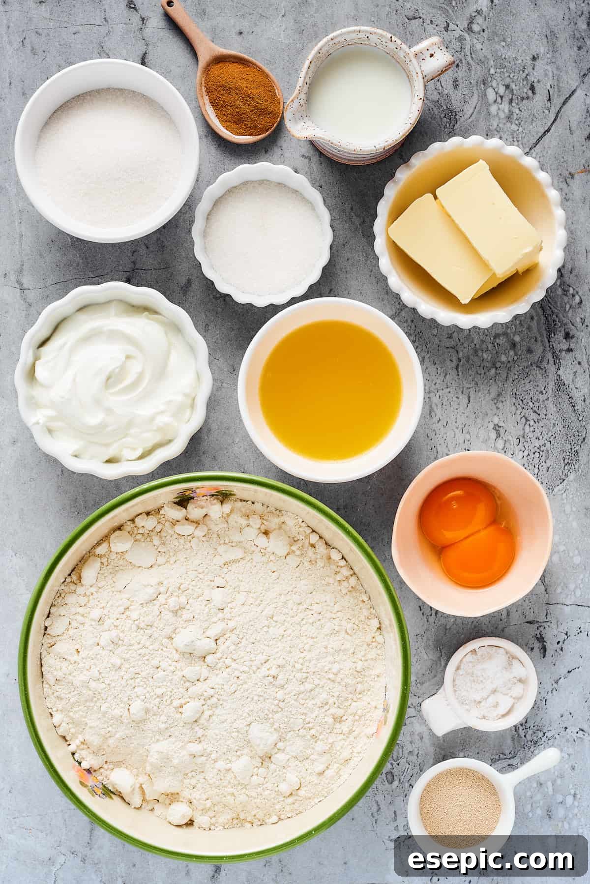 From top left: Sugar, cinnamon, milk, granulated sugar, butter, heavy cream, melted butter, melted butter, egg yolks, spelt flour, salt, instant yeast, neatly arranged ingredients for cinnamon rolls.