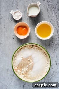 Dry baking ingredients mixed in a large mixing bowl. Sugar, milk, egg yolks, and melted butter are near the bowl in separate dishes, ready to be combined.