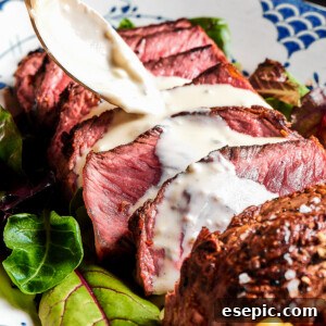 Sliced blue steak with creamy sauce being spooned over the top, showcasing its perfect doneness.