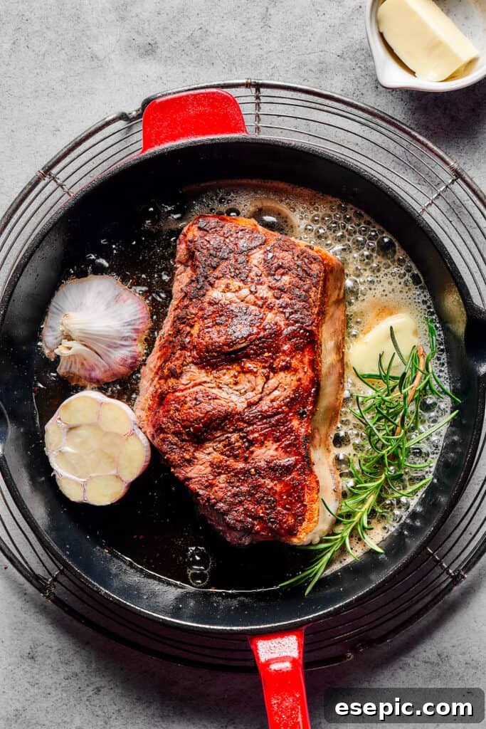 A pristine sirloin steak sizzling in a cast-iron pan, surrounded by melting butter, a fragrant sprig of rosemary, and a halved head of garlic.