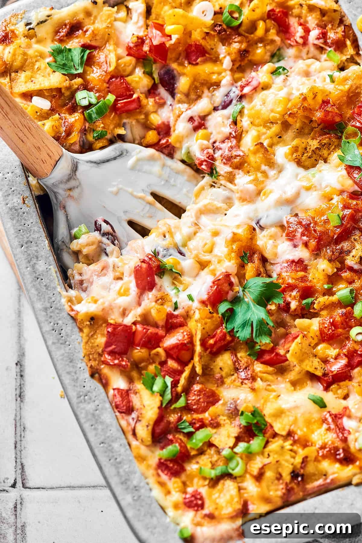 A serving utensil in a large baking pan of cheesy chicken bake, showing the melted cheese and layers.