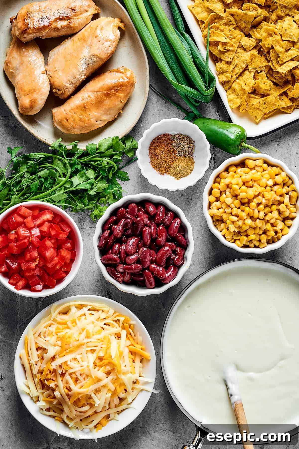 From top: Cooked chicken breast, green onions, crushed chips, seasonings, chopped tomatoes, beans, corn, cheese, white sauce, illustrating the layers of the casserole.