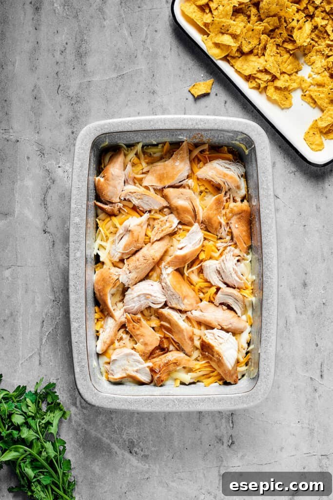 Cheese and chicken layered over other ingredients in a baking dish.