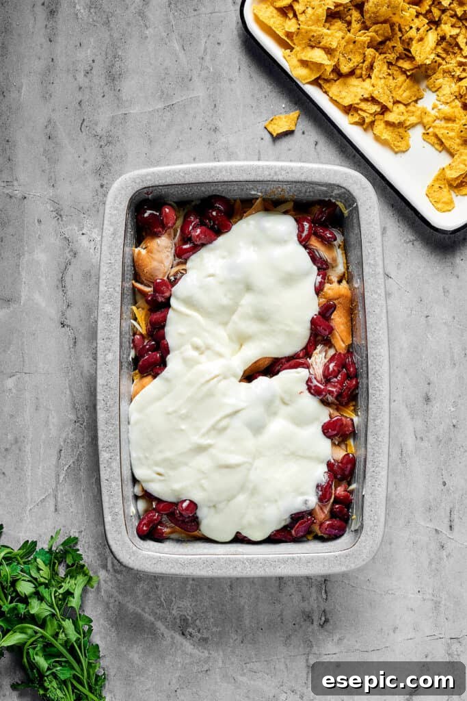 Spicy Fiesta Chicken Bake 8 Beans, creamy white sauce, tender chicken, and other delicious ingredients forming distinct layers in a rectangular baking pan.
