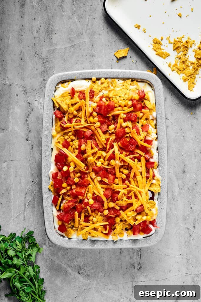 An unbaked casserole topped with chopped tomatoes and shredded cheese.