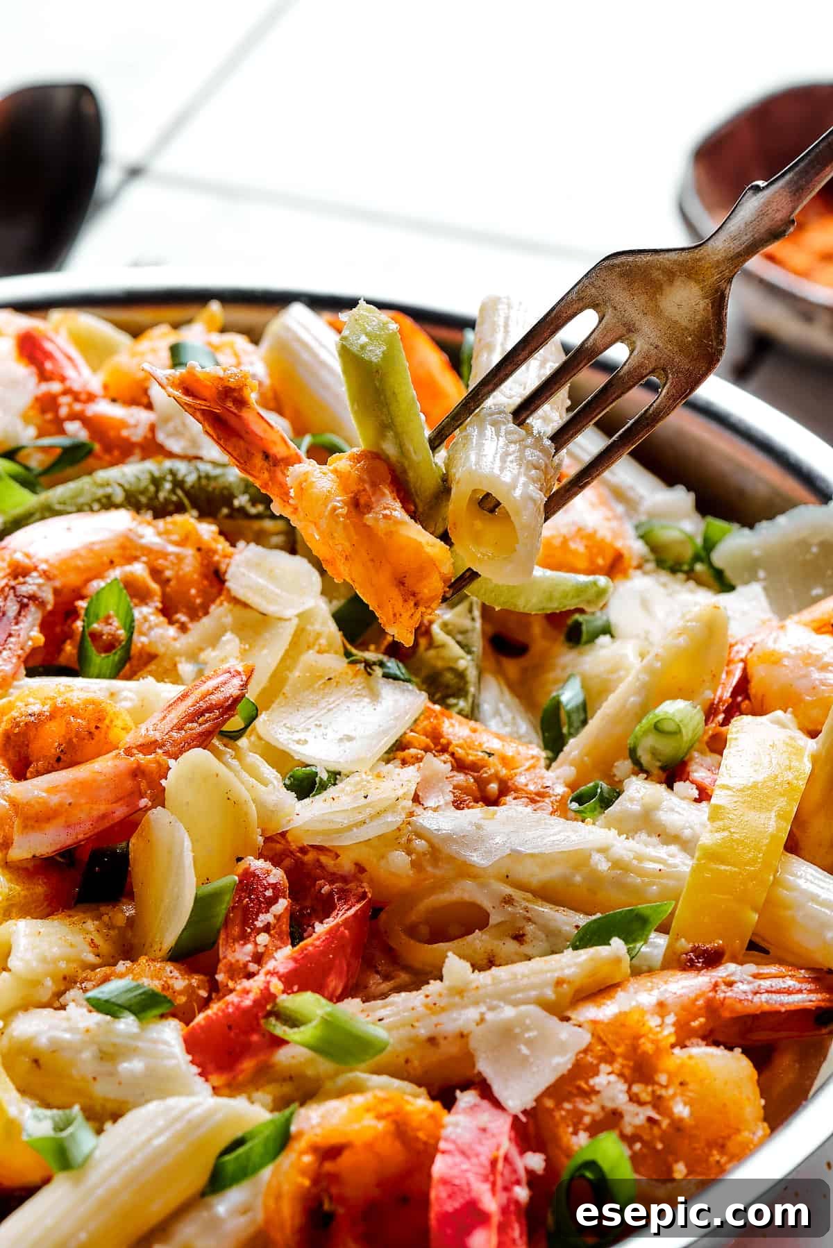 A fork lifting a portion of creamy Rasta Pasta with bell peppers and shrimp from a serving dish, highlighting the inviting texture and vibrant ingredients.