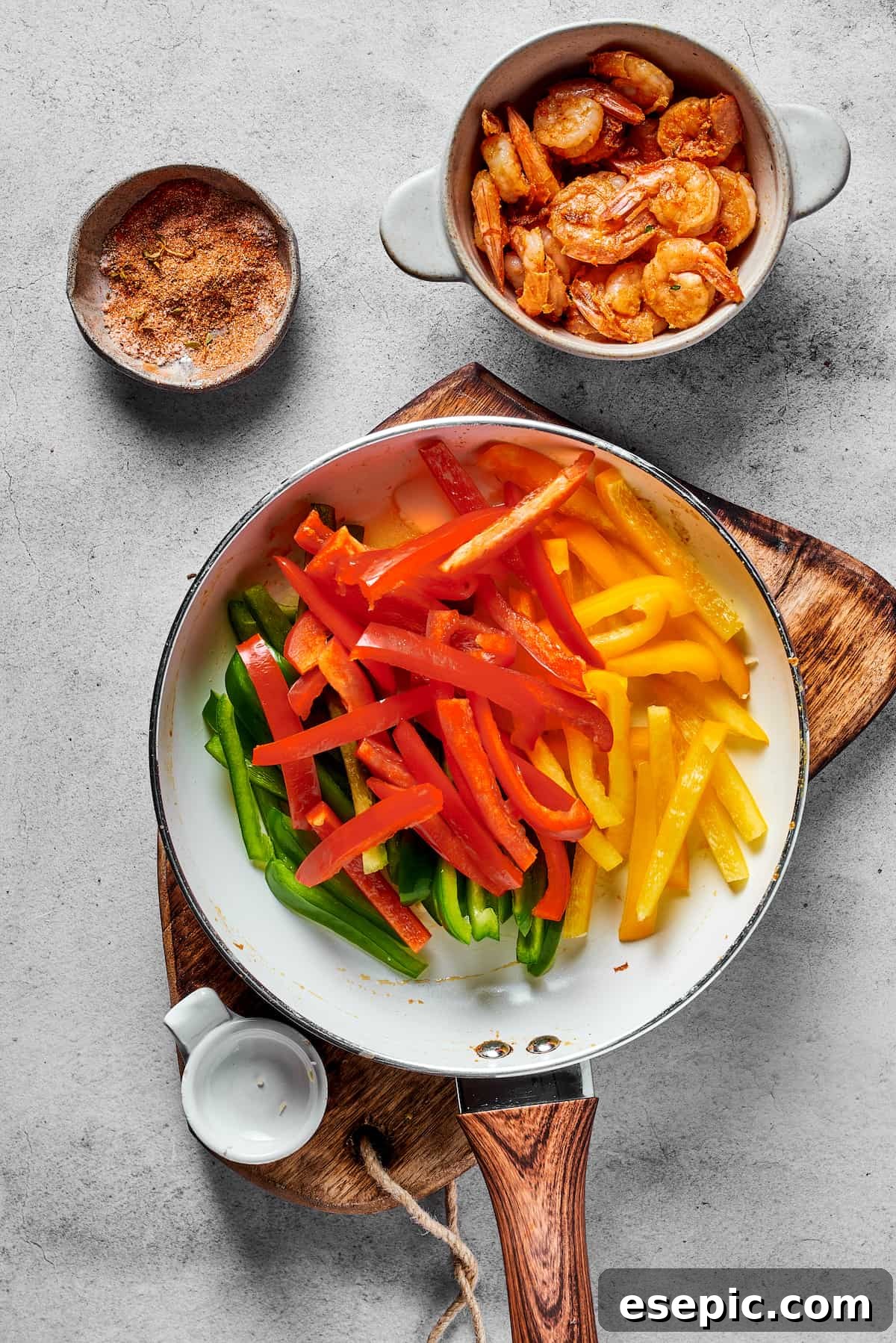 Red, yellow, and green bell pepper slices cooking in a skillet, next to a bowl of seasoned and cooked shrimp, ready to be combined into the Rasta Pasta.